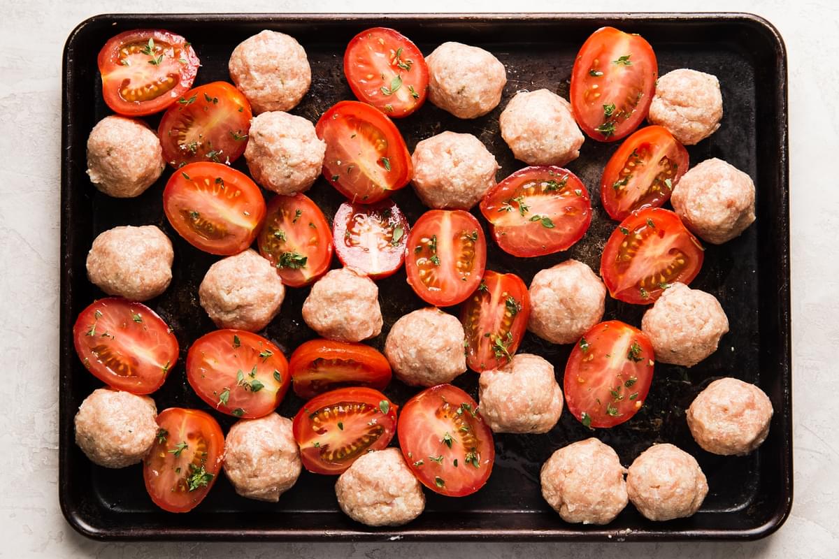 Italian chicken meatballs and roma tomatoes on a baking sheet