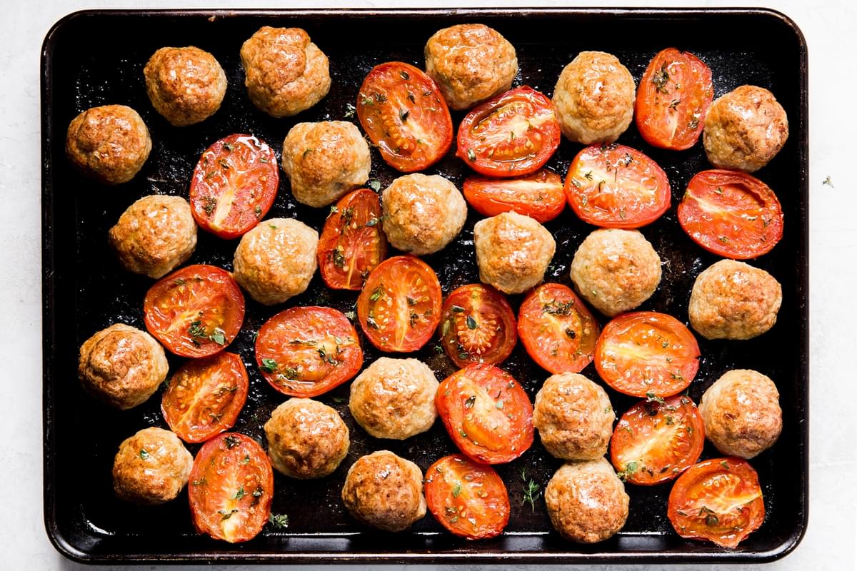 Italian chicken meatballs with roasted tomatoes on a baking sheet