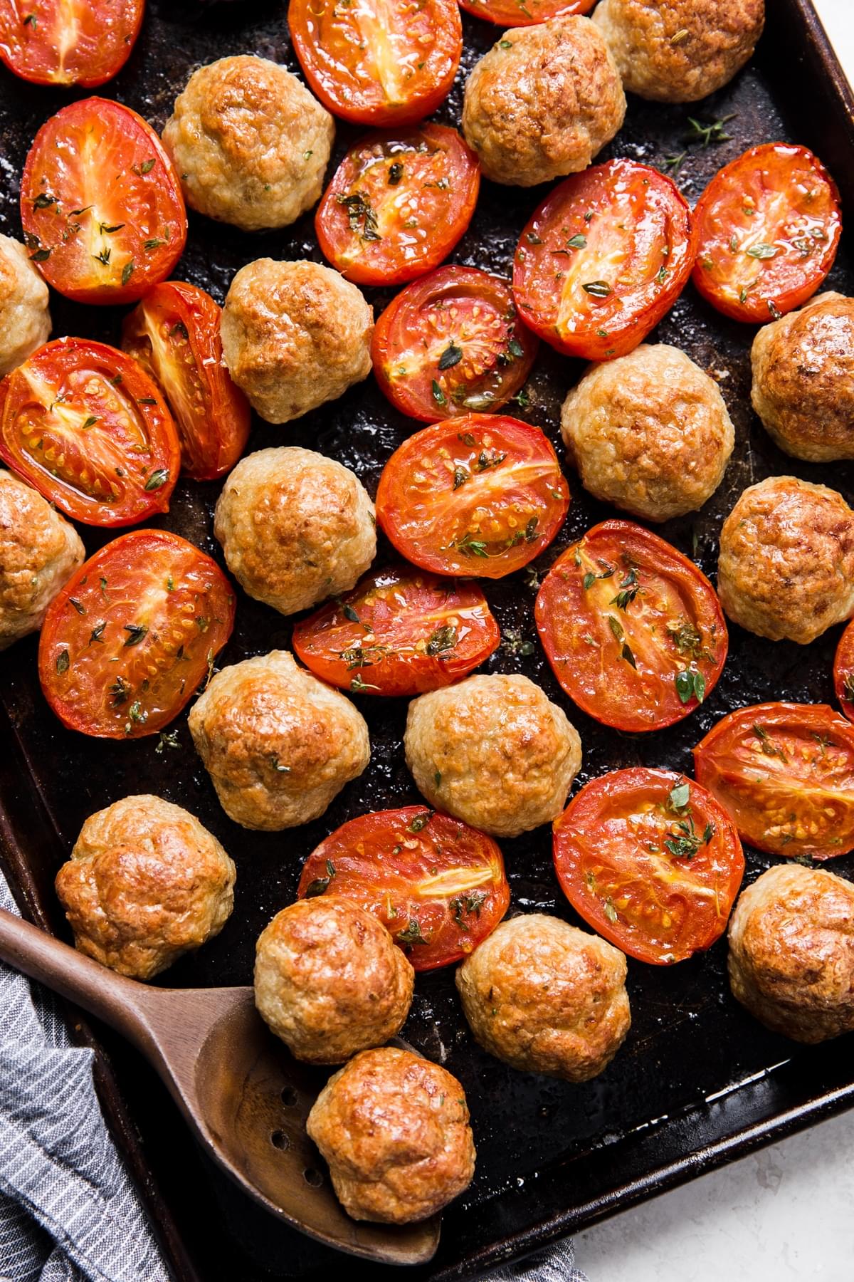 Italian chicken meatball and roasted tomatoes on a baking sheet with a serving spoon