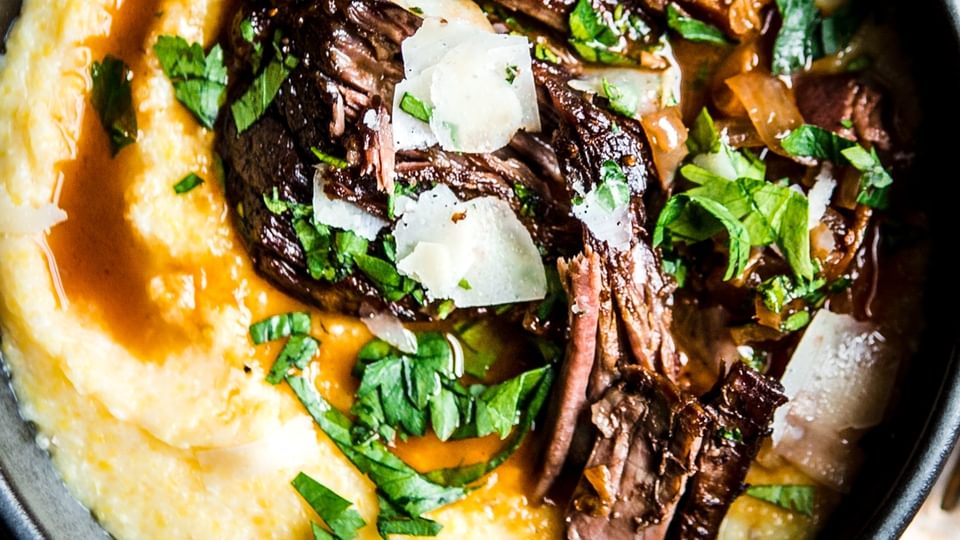 Italian pot roast served over polenta in a black bowl garnished with parsley