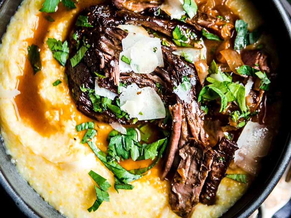 Italian pot roast served over polenta in a black bowl garnished with parsley