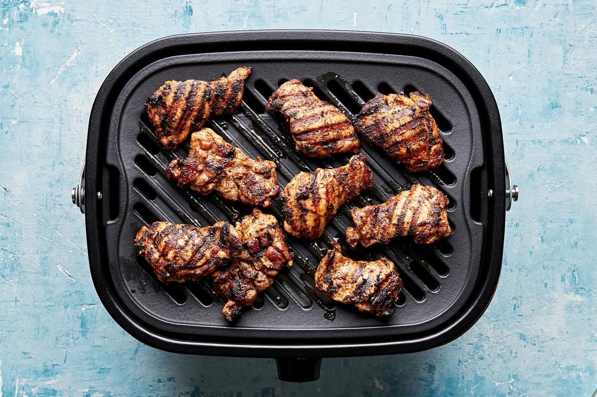 jerk marinated chicken thighs being cooked on a grill