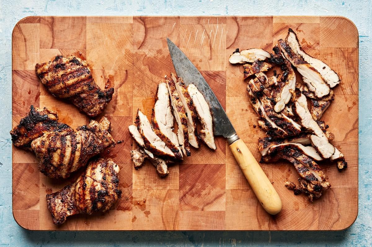 grilled jerk chicken thighs being sliced on a cutting board