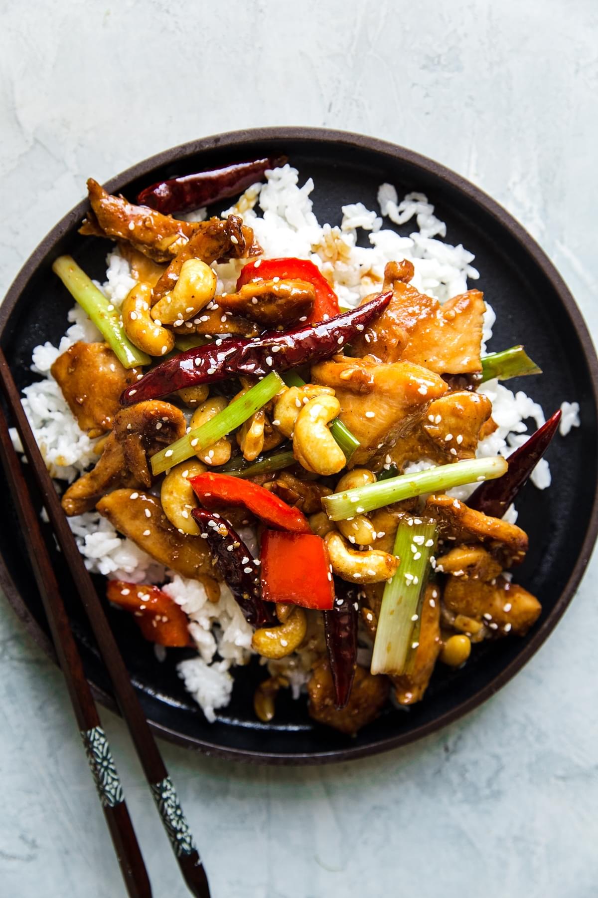 kung pao chicken over white rice on a plate with chop sticks