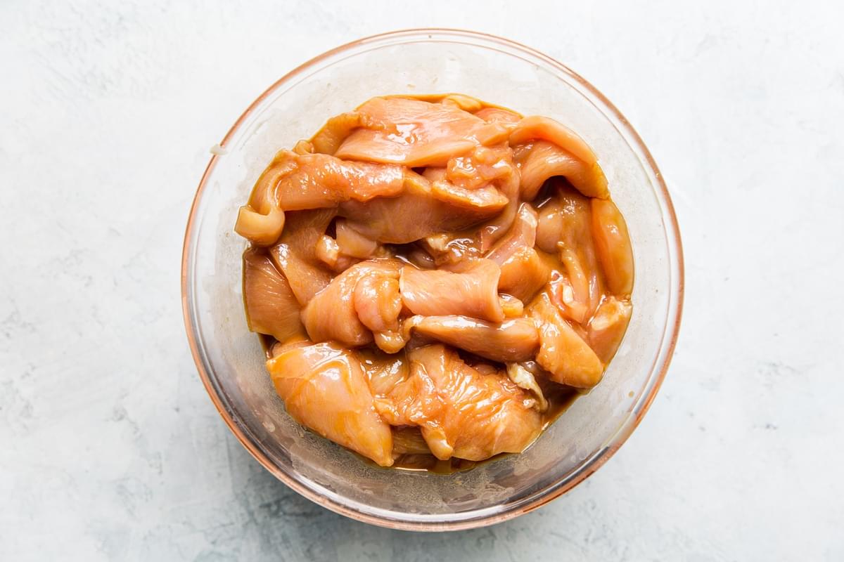 thinly sliced raw chicken breast in a glass bowl with a kung pao marinade
