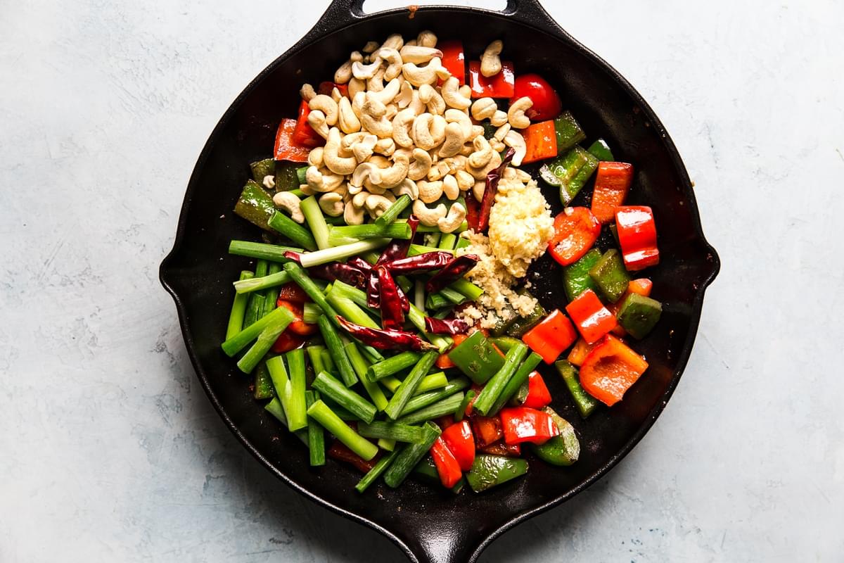 bell peppers, green onions and cashews in a cast iron skillet for kung pao chicken