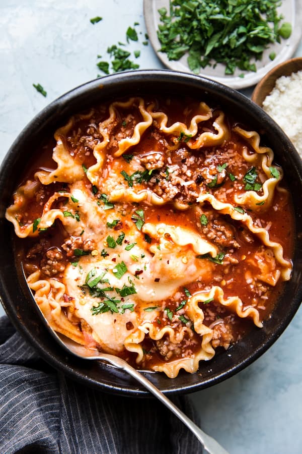 Cheesy lasagna soup with ground beef in a black bowl with a spoon.