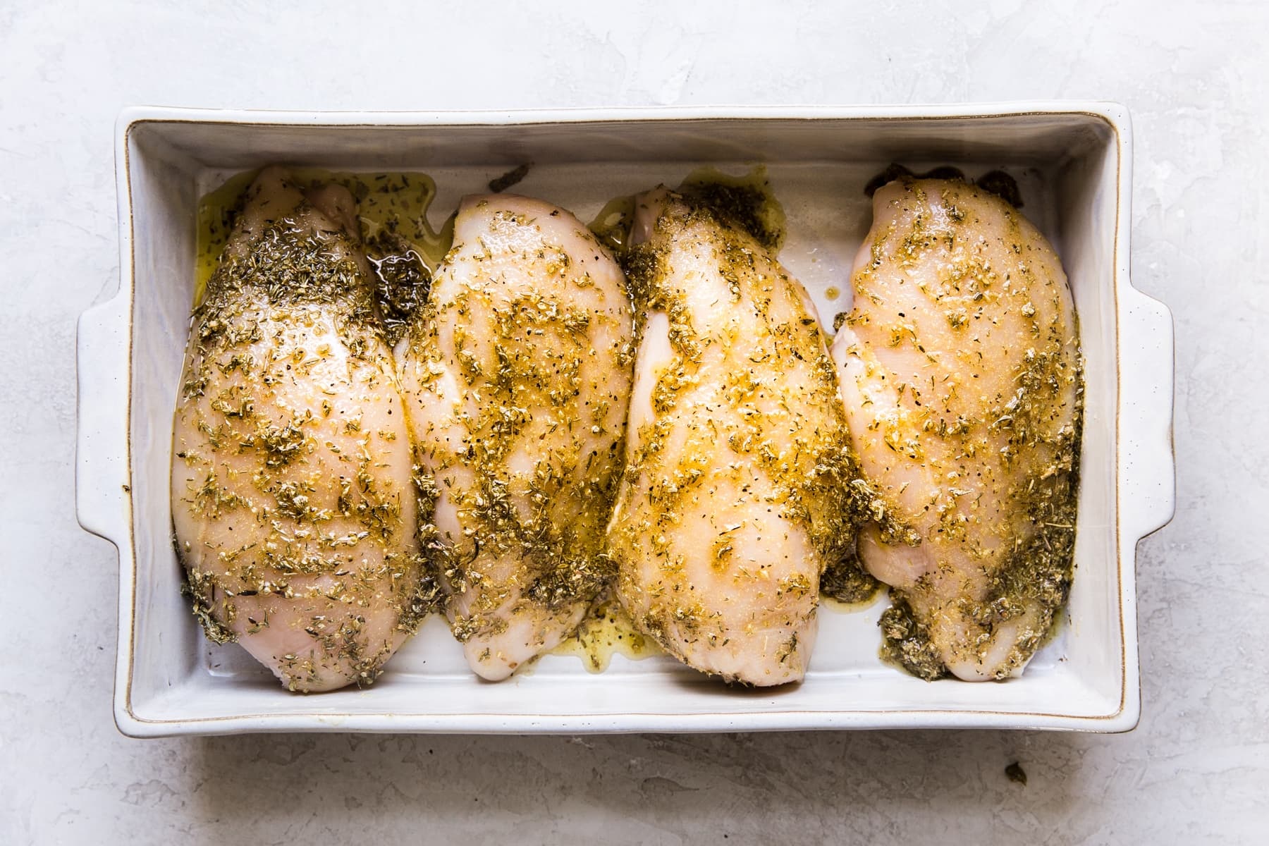 4 chicken breasts with olive oil and spices in a baking dish.