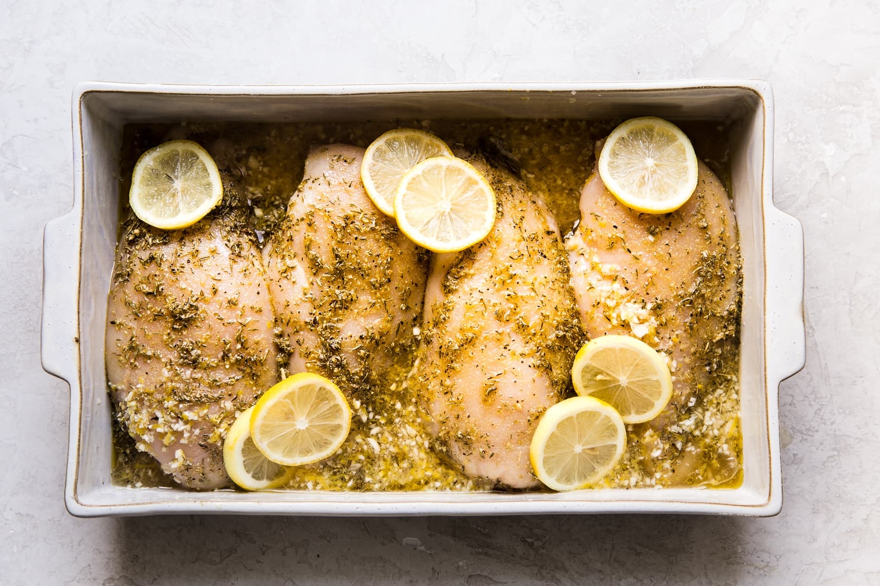 lemon chicken breast in a baking dish with herbs and lemon juice and lemon slices