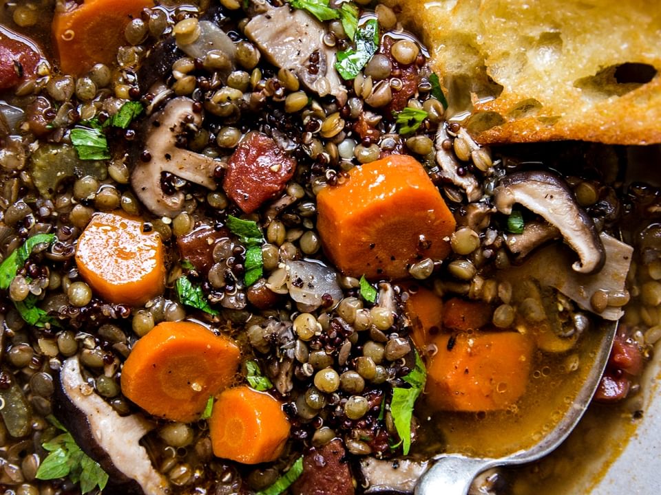 lentil stew with quinoa and mushrooms in a ceramic bowl with crusty buttered bread.