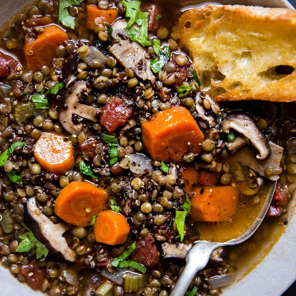 lentil stew with quinoa and mushrooms in a ceramic bowl with crusty buttered bread.