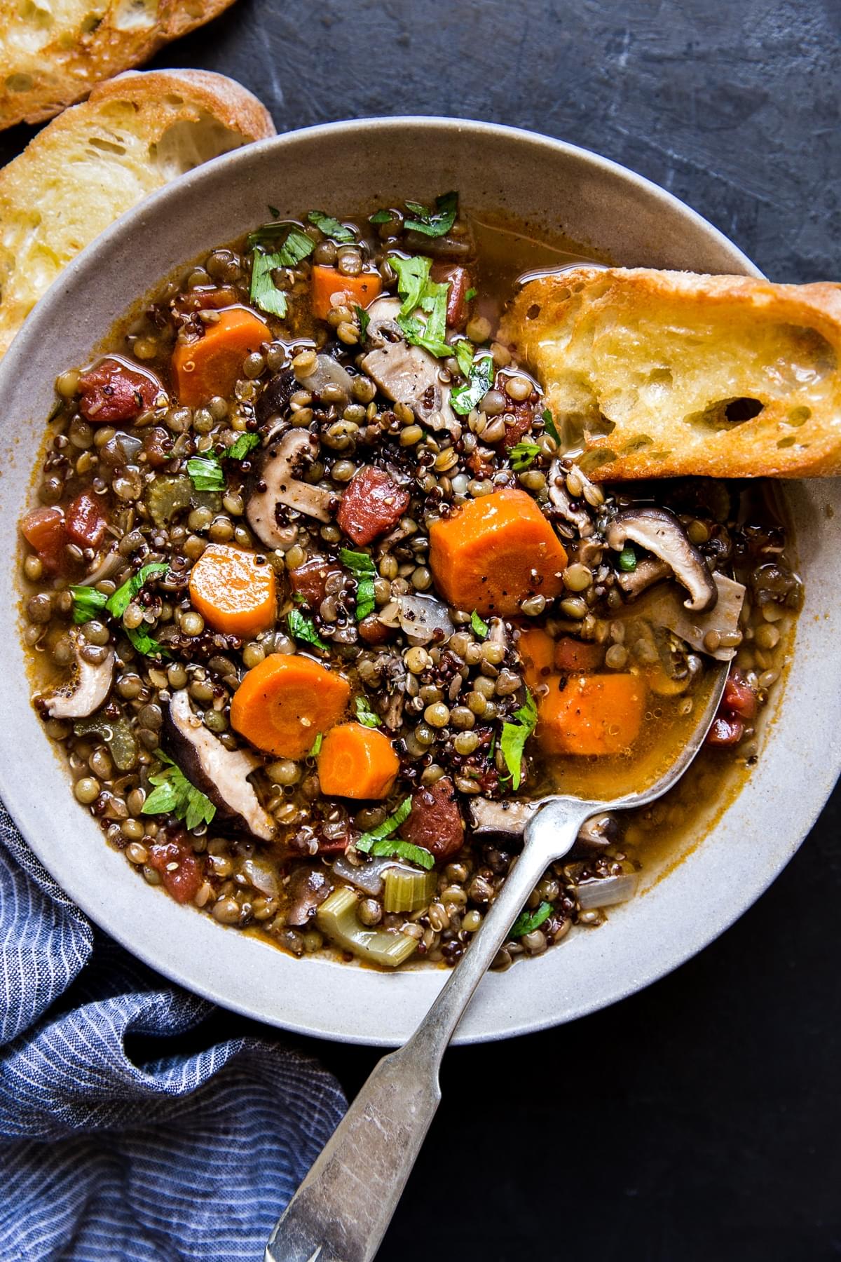 bowl of lentil stew with quinoa and mushrooms with a side of crusty buttered bread