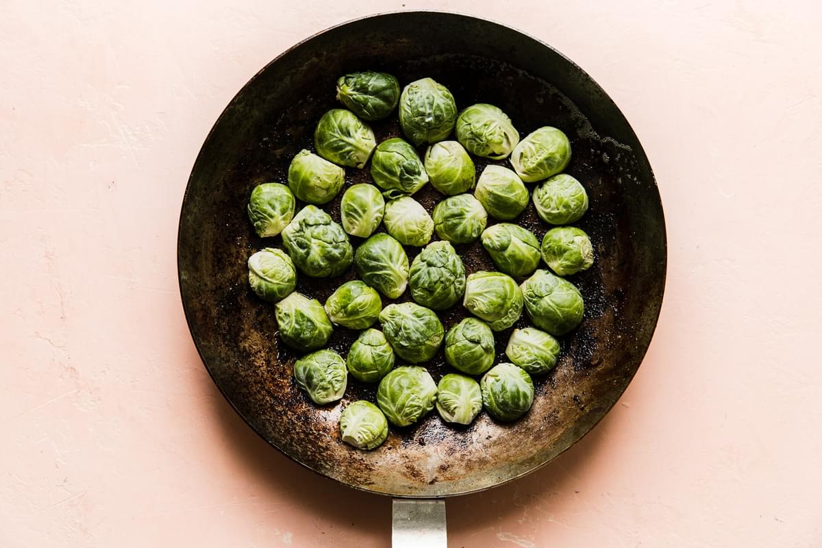 brussels sprout halves being cooked cut side down in a cast iron skillet