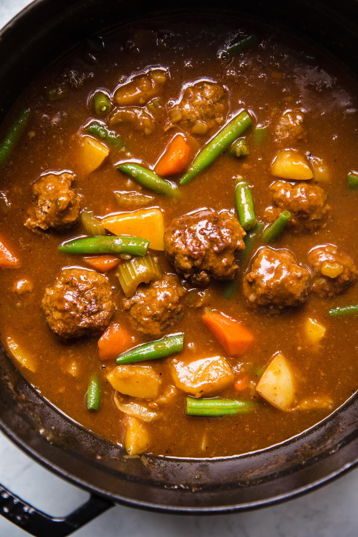 homemade meatball stew with green beans, celery, carrots, onion, potatoes and ground beef in a pot on the counter