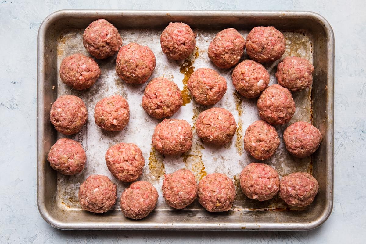 golf ball sized home made meatballs rolled on a baking sheet sitting on the counter