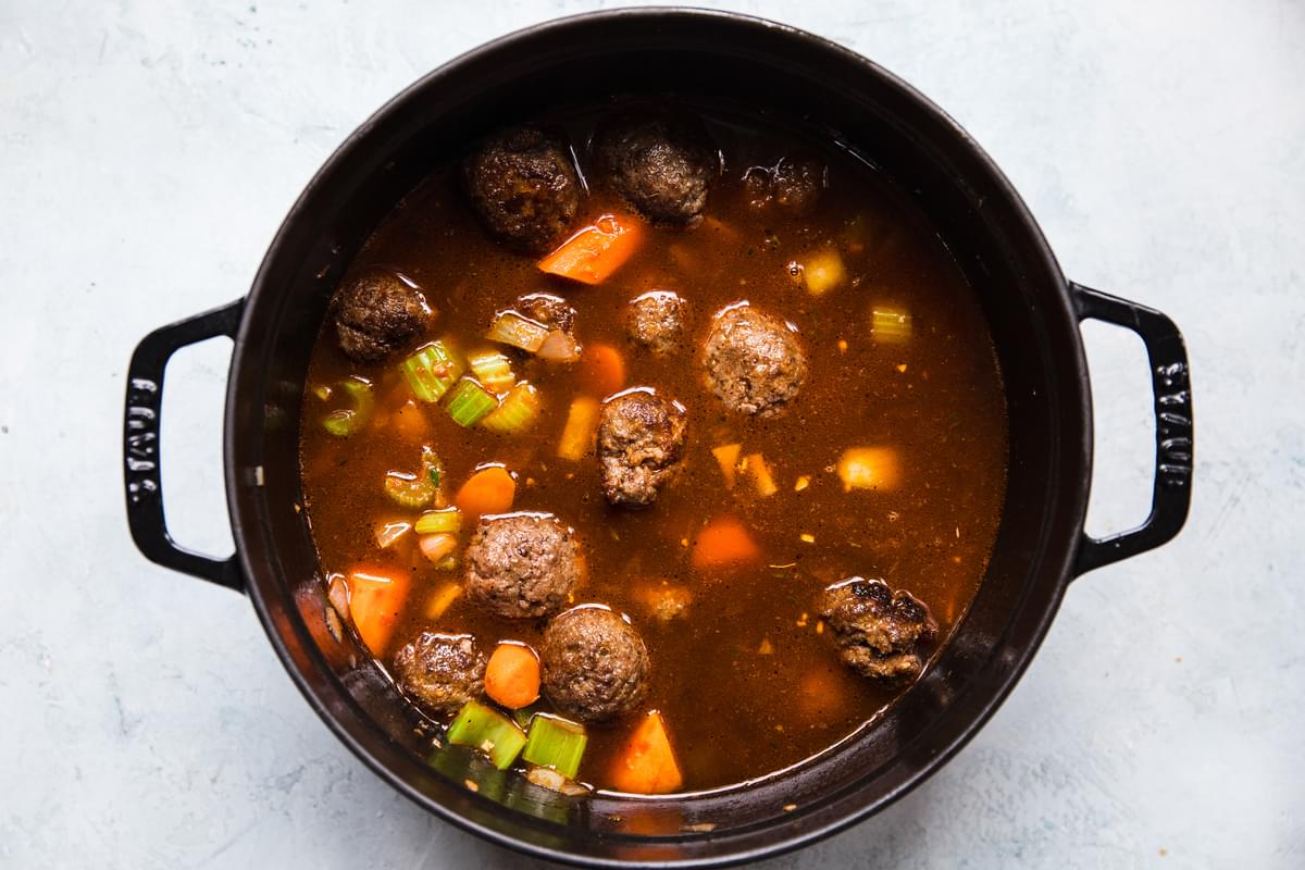 cooked vegetables, tomato paste, thyme, beef stock, beef bouillon and meatballs in a pot for meatball stew