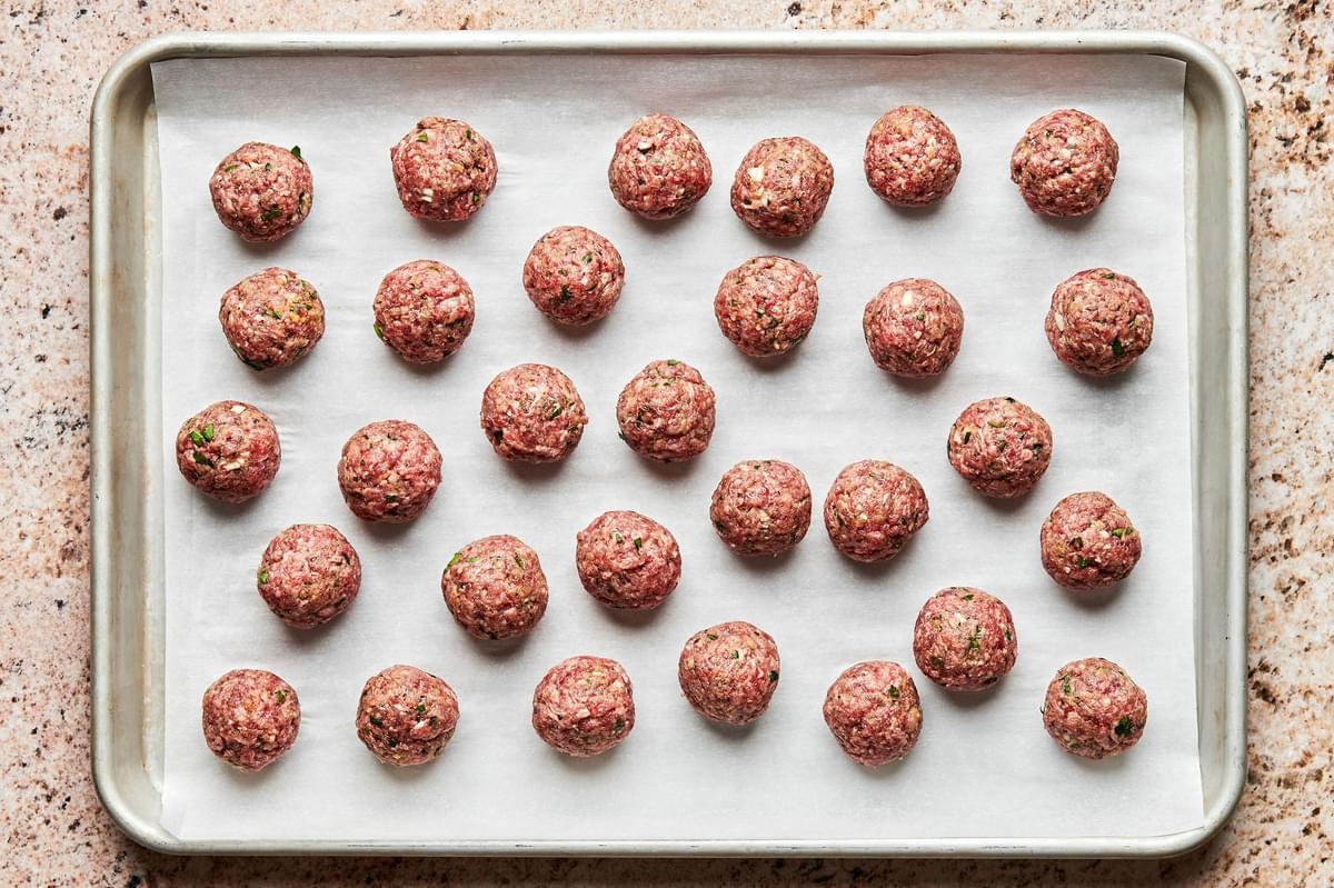 raw meatballs on a baking sheet made with ground beef, egg, Worcestershire, breadcrumbs, parsley, parmesan, garlic & spices