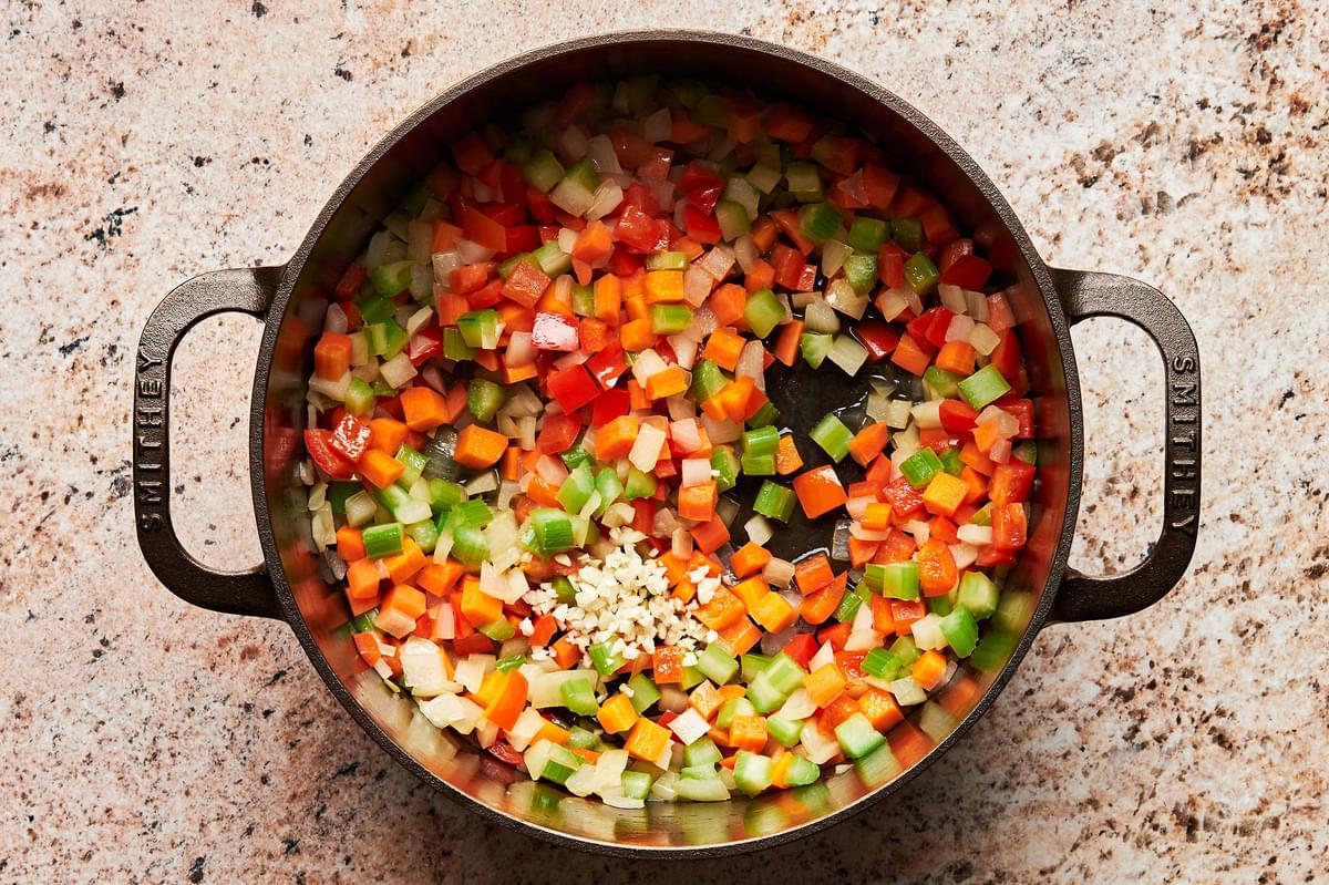 chopped onion, celery, carrots, and bell pepper being cooked in olive oil in a soup pot