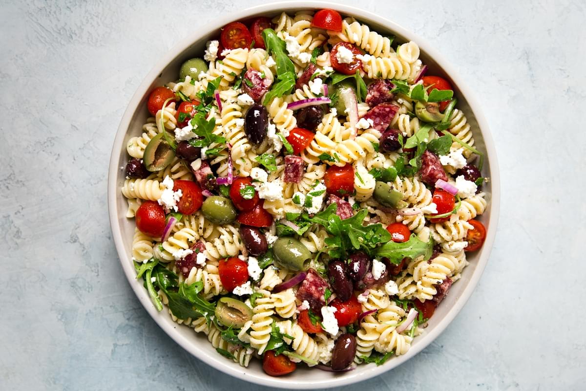 Mediterranean Pasta Salad in a bowl with feta, olives, tomatoes and arugula and salami