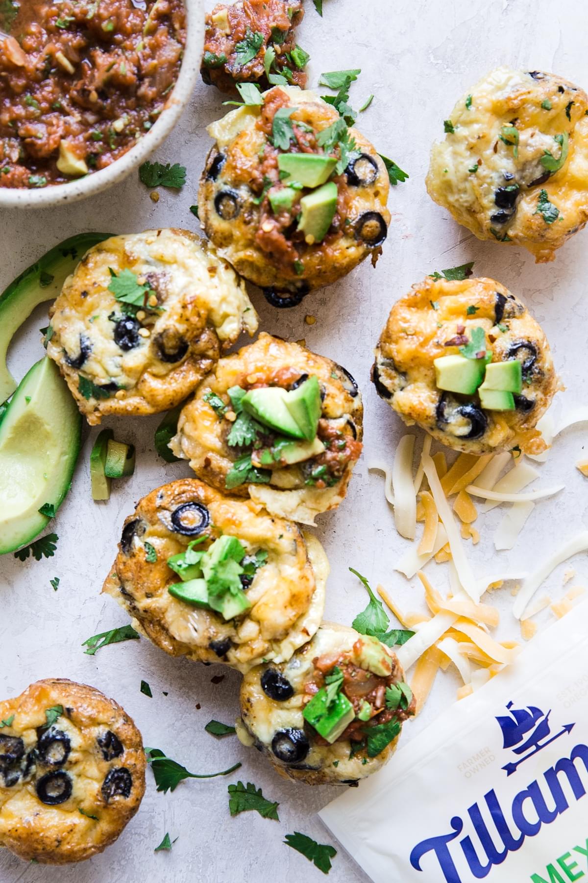 Egg and sausage muffins topped with avocado, olives and grated cheese