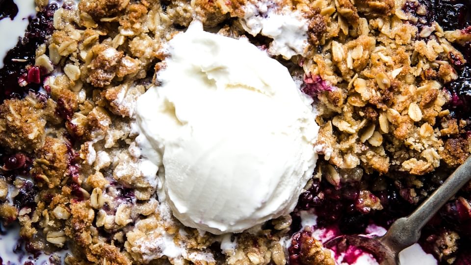pie tin filled with mixed berry crisp and topped with a scoop of vanilla ice cream