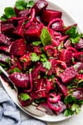 Moroccan beet salad with red onions and fresh herbs on a white platter with a spoon