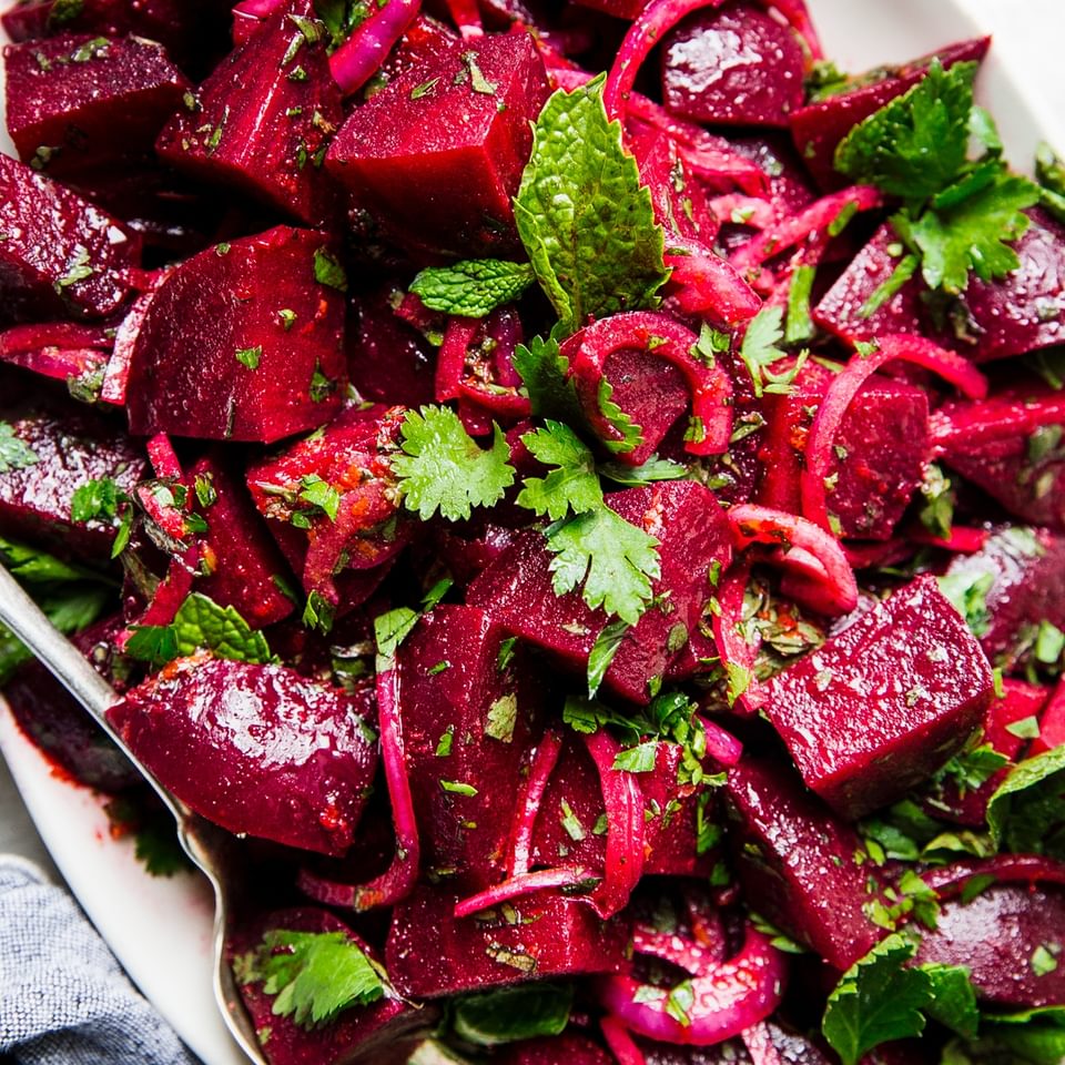 Moroccan beet salad with red onions and fresh herbs on a white platter with a spoon