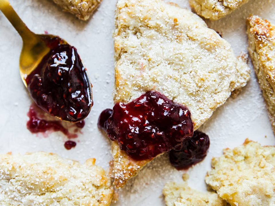 homemade oat scones on a white surface with a spoonful of raspberry jam