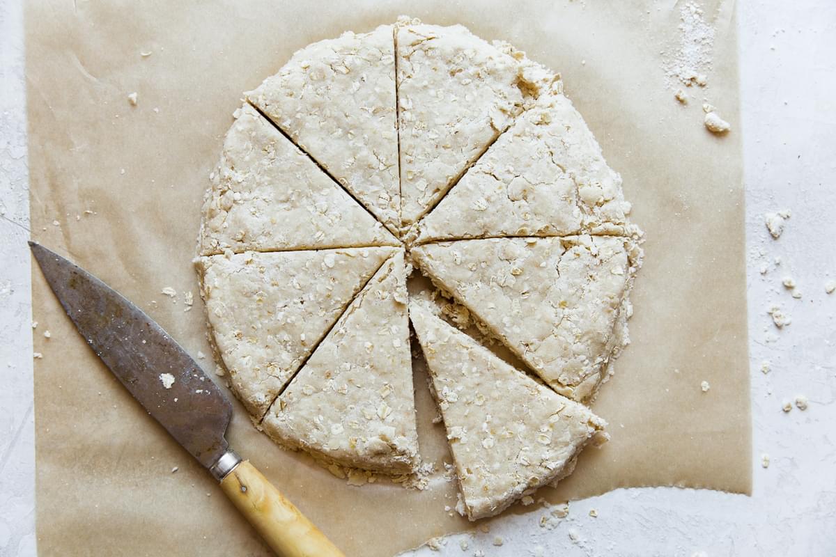 oat scone dough pressed into a circle on parchment with a sharp knife cut into triangles
