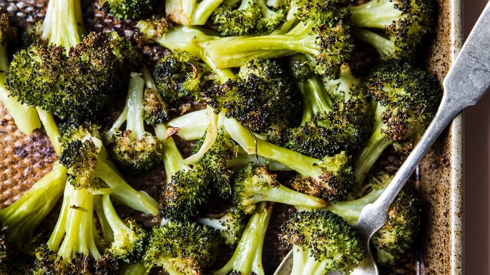 oven baked broccoli on a baking sheet with a serving spoon