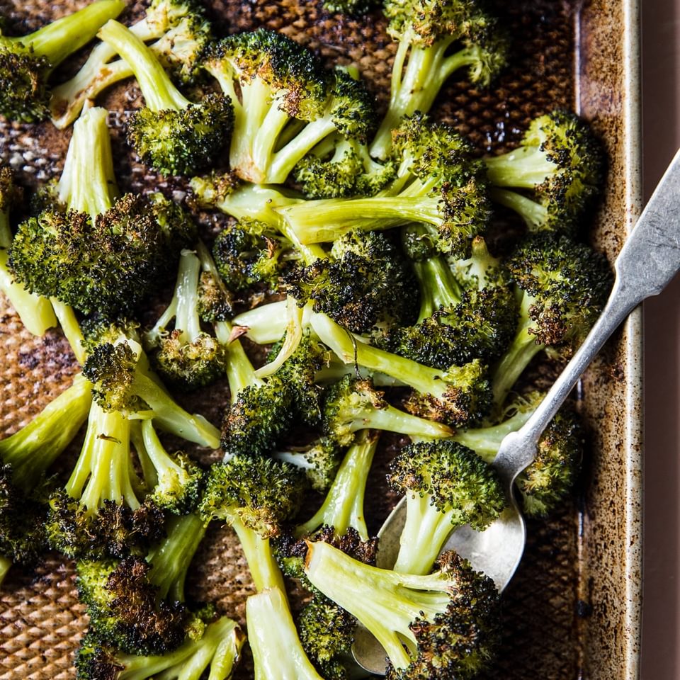 oven baked broccoli on a baking sheet with a serving spoon