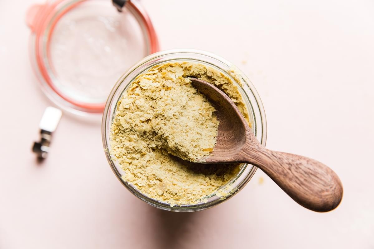 Nutritional yeast in a glass jar with a wooded scoop