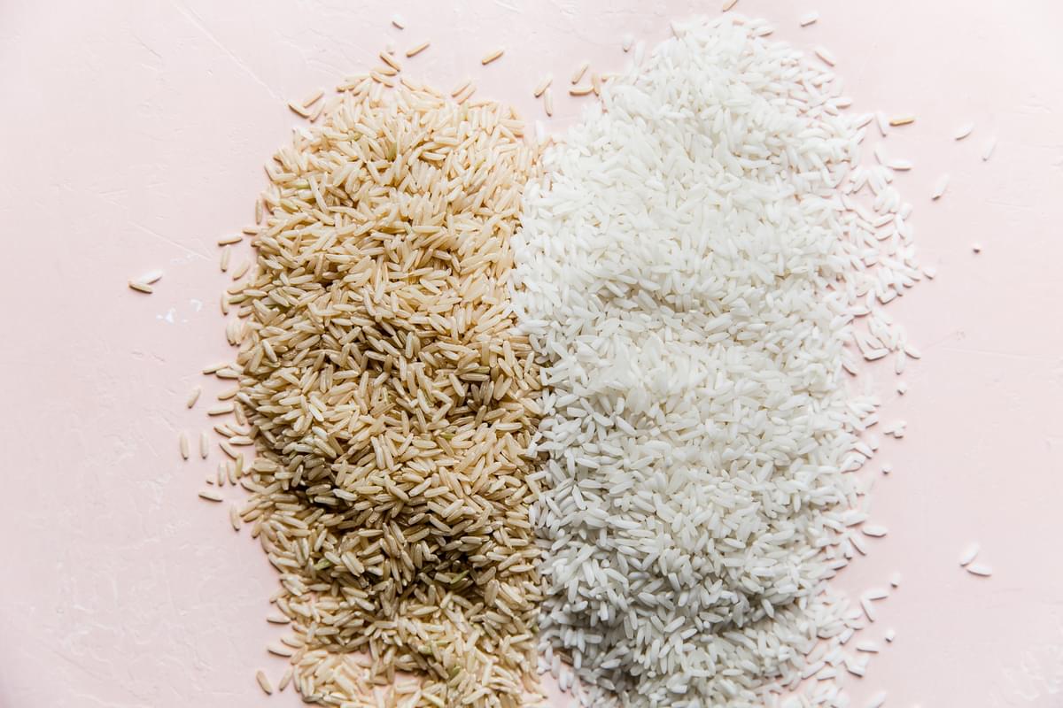 uncooked white rice and brown rice on a light pink surface
