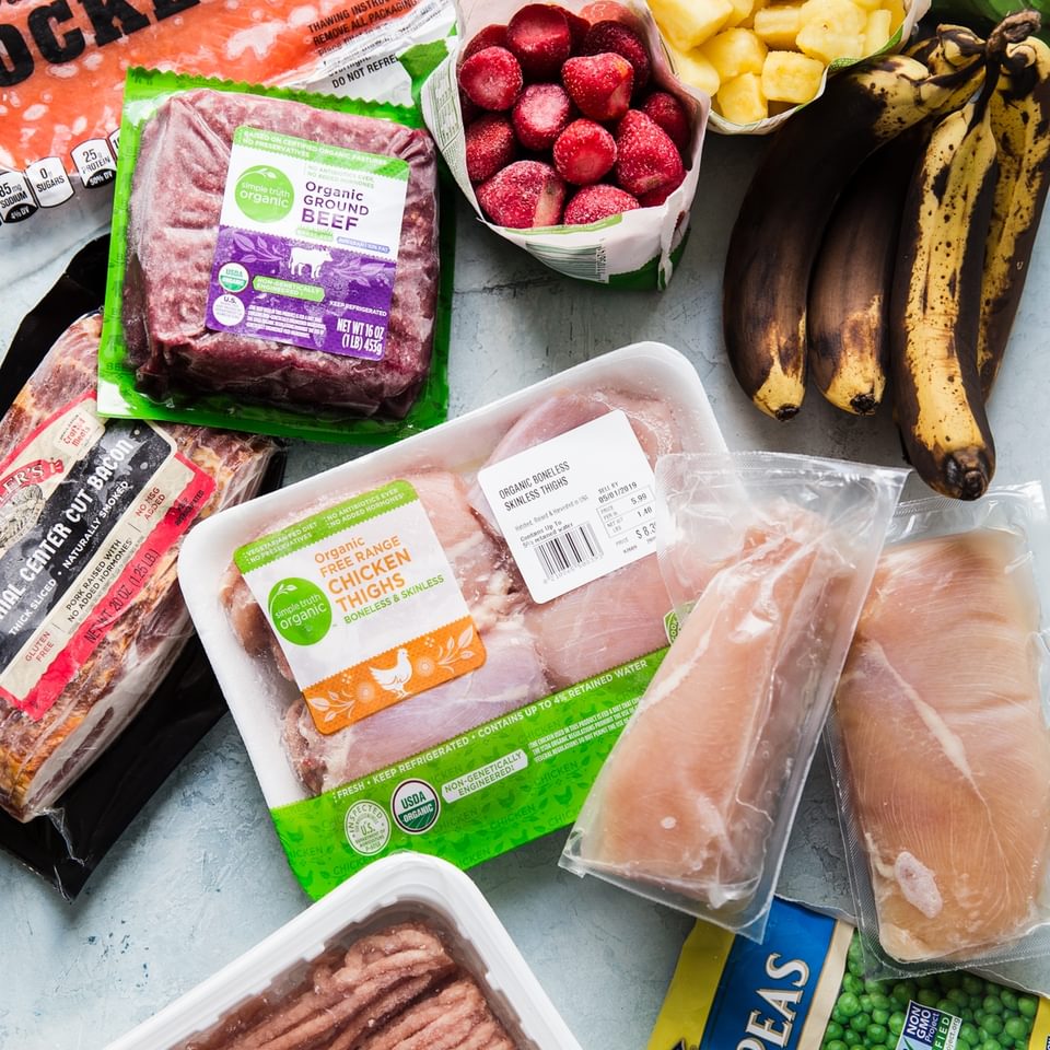 frozen chicken thighs, frozen ground beef, frozen fruit and frozen vegetables spread out on a blue surface