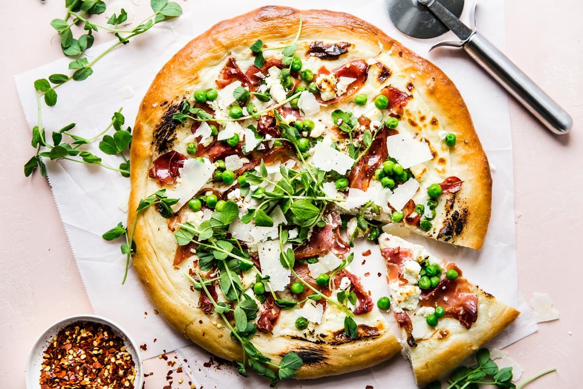 Pea and prosciutto pizza with goat cheese cream sauce parmesan cheese spring pizza with slice taken out