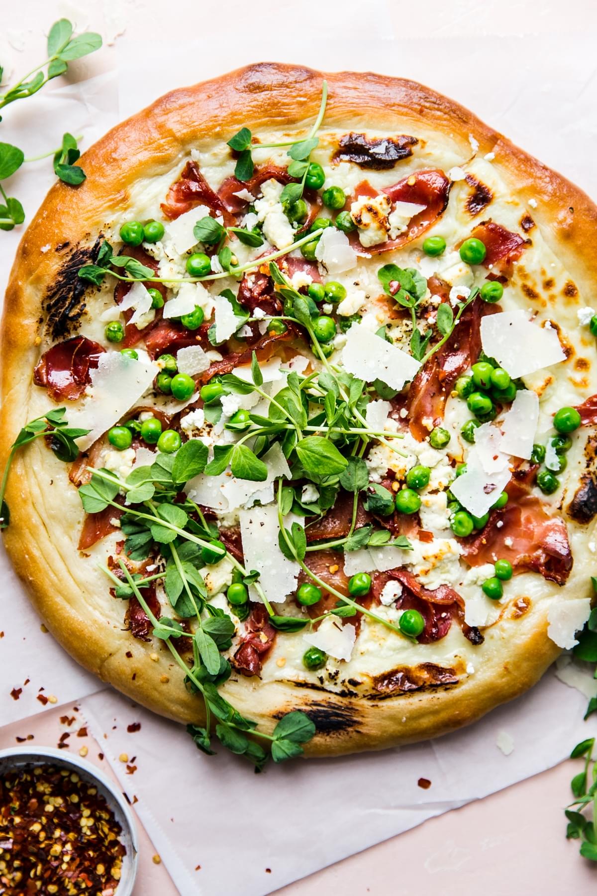 Pea and prosciutto pizza with goat cheese cream sauce parmesan cheese spring pizza with micro greens and pepper flakes