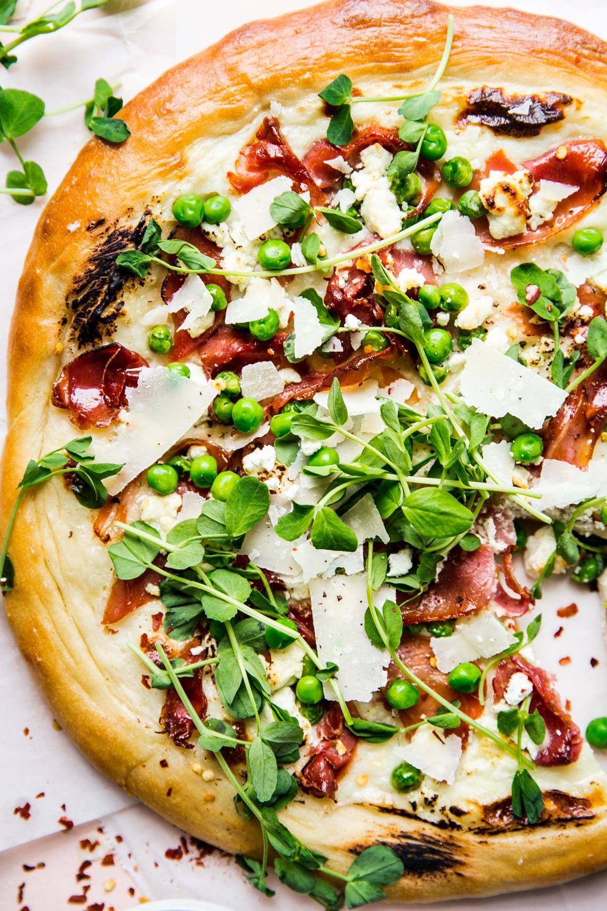 Pea and prosciutto pizza with goat cheese cream sauce parmesan cheese spring pizza with micro greens and pepper flakes