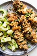Peanut Sauce Marinated Chicken Skewers on a plate with cucumber salad
