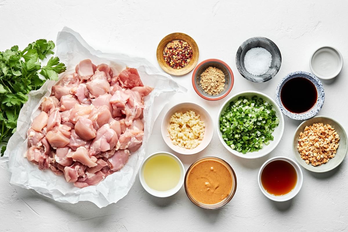 raw chicken pieces, cilantro, peanut butter, soy sauce, sesame oil, vinegar, chicken, fresh herbs, and spices in prep bowls