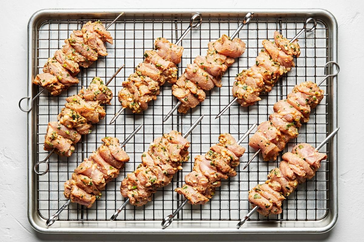 peanut sauce marinated chicken thighs on skewers on top of a cooling rack placed in a baking sheet