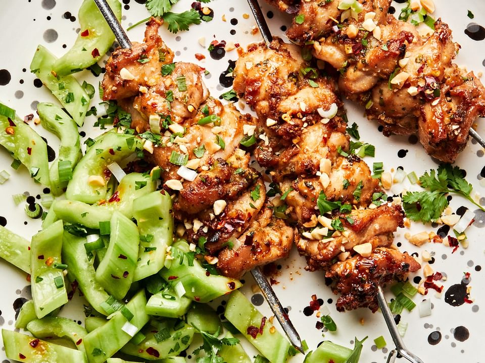Peanut Sauce Marinated Chicken Skewers sprinkled with crushed peanuts on a plate served with cucumber salad