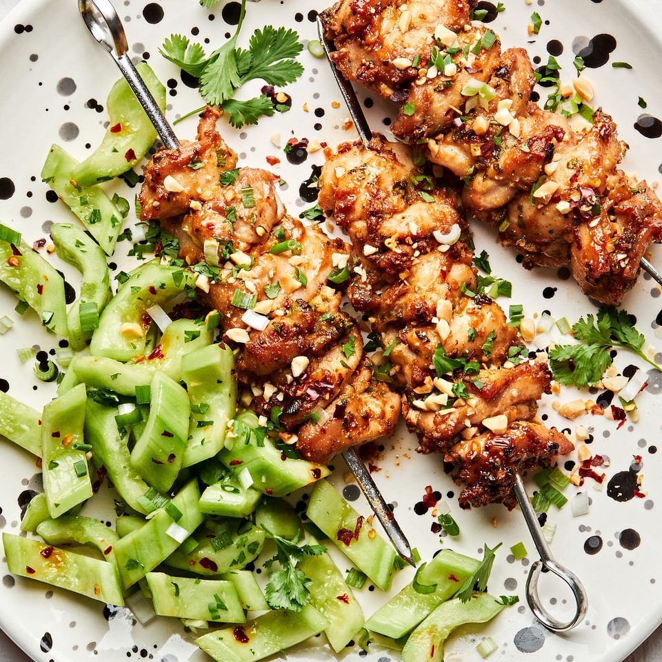 Peanut Sauce Marinated Chicken Skewers sprinkled with crushed peanuts on a plate served with cucumber salad