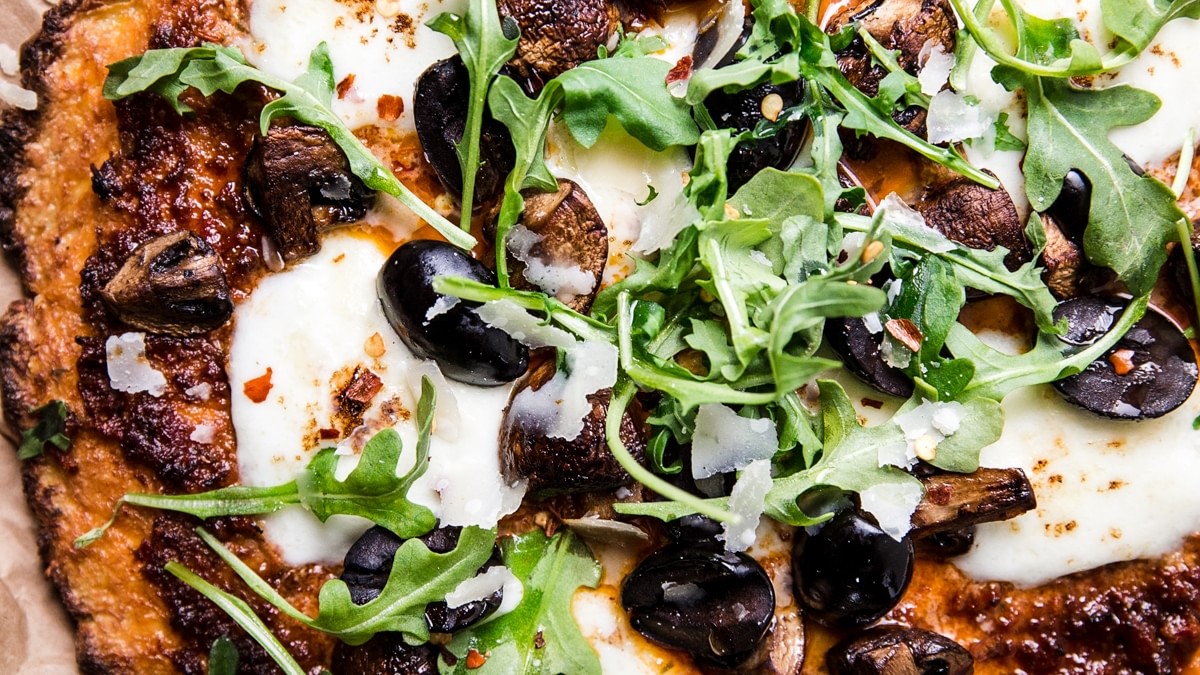 Cauliflower pizza crust pizza with olives, arugula, mozzarella and parmesan cheese