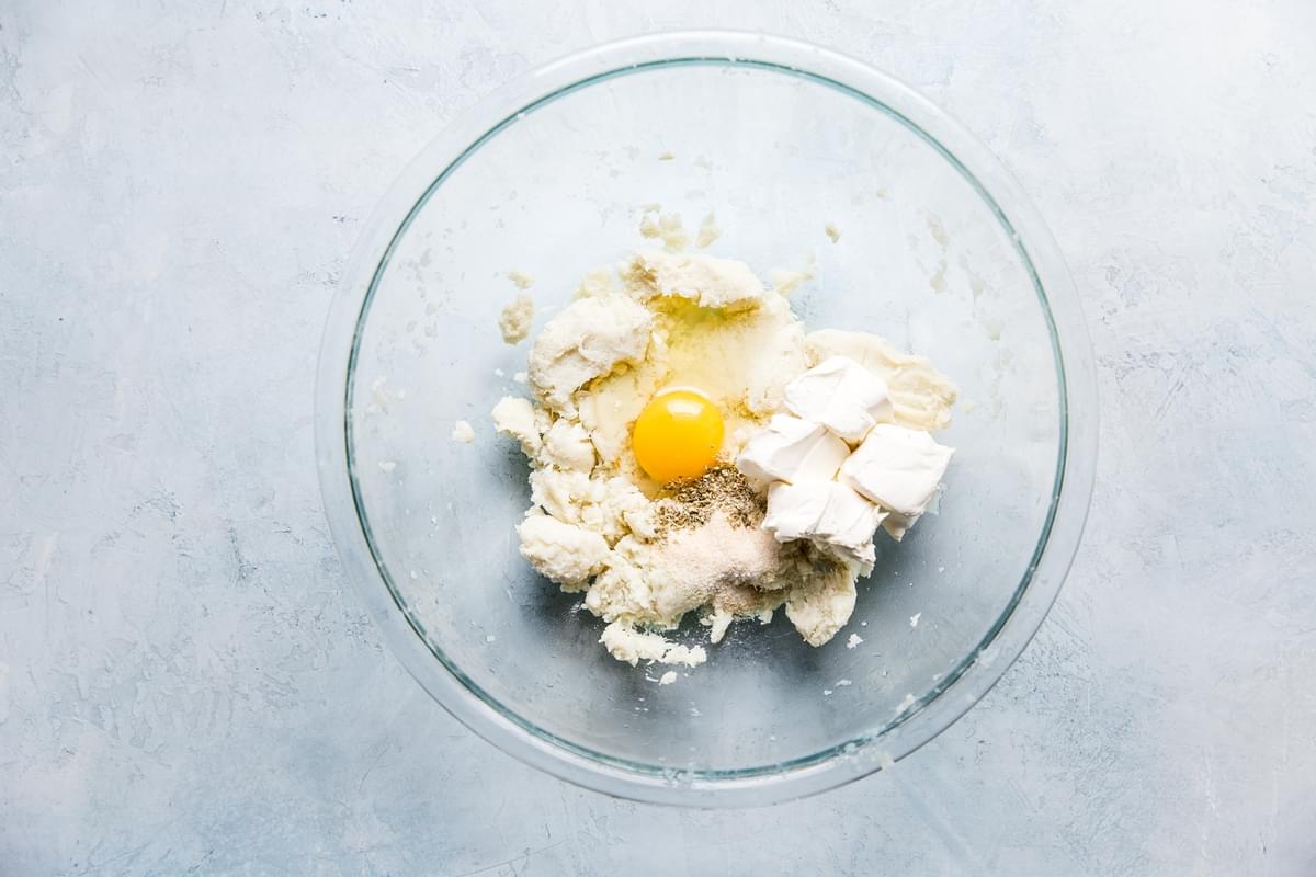 crumbled cooked cauliflower, 1 egg and cream cheese in a bowl