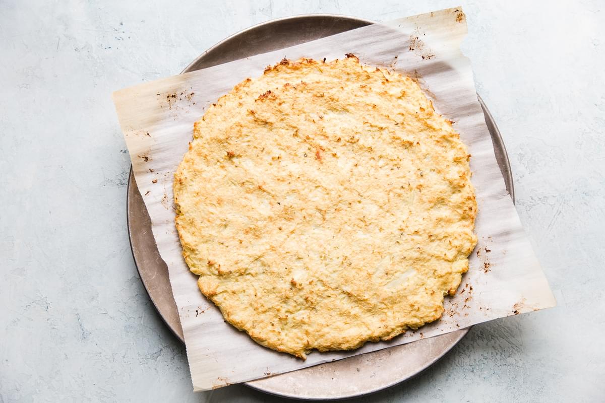 Par cooked cauliflower pizza crust on a parchment on a pizza pan
