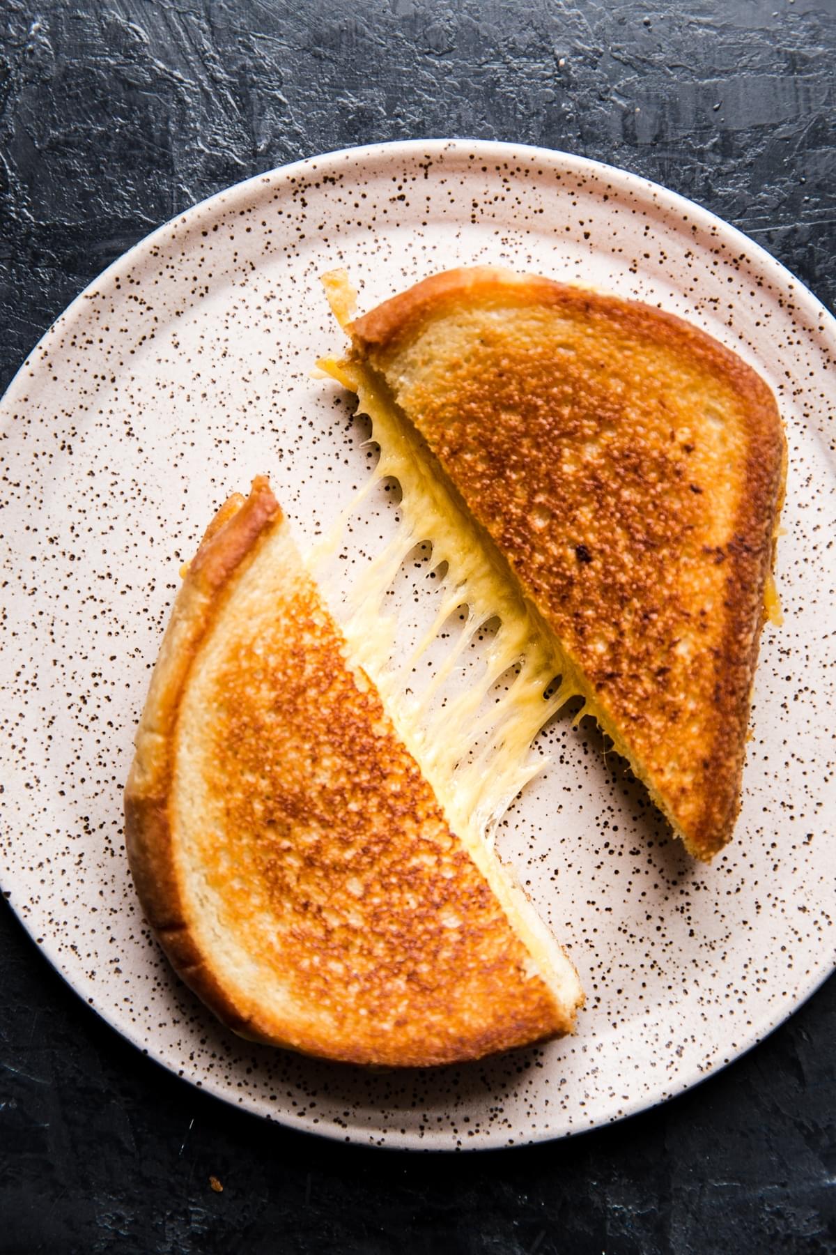 pink speckled plate with two grilled cheese halves showing melted cheese