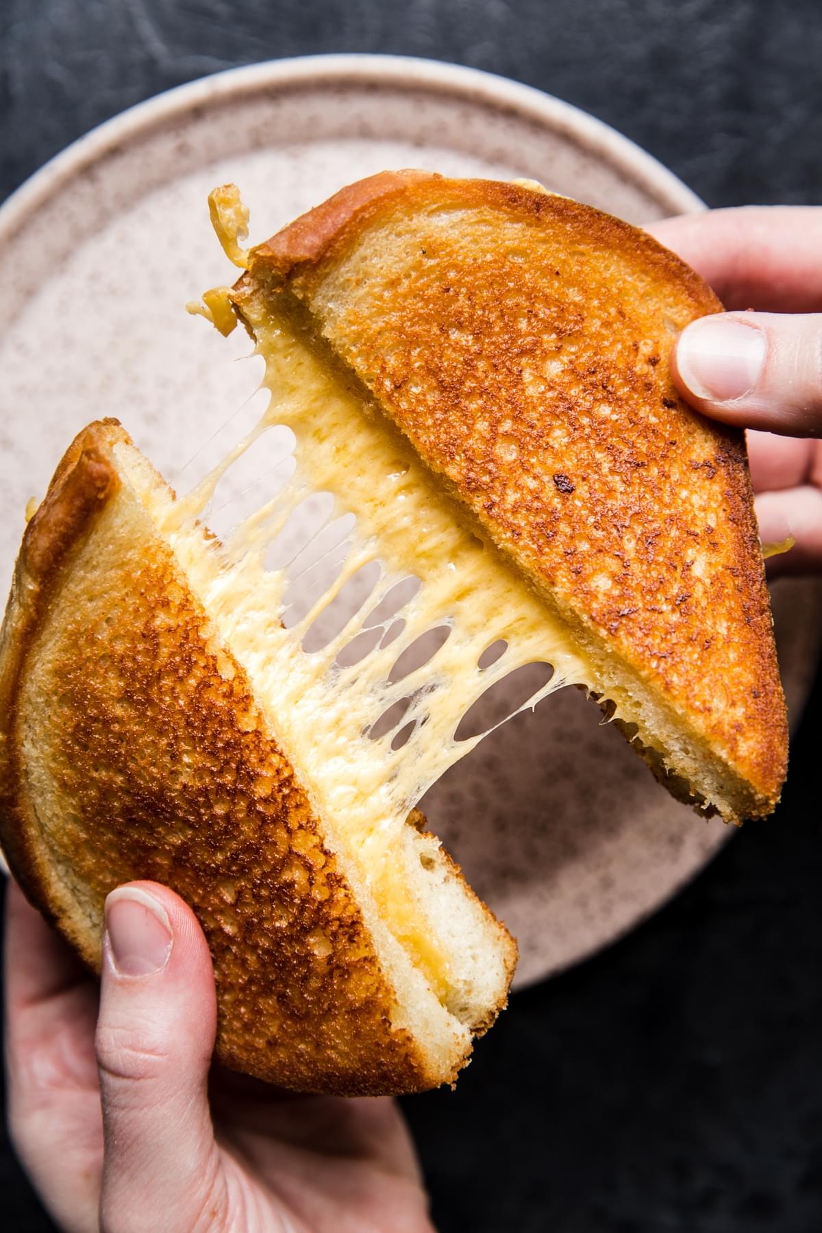 hands pulling apart two halves of grilled cheese showing melted cheese