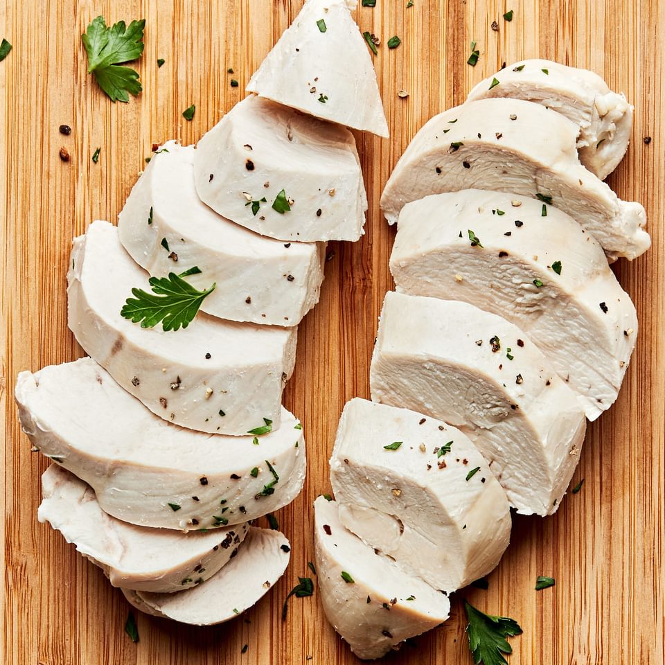 perfect poached chicken sliced on a cutting board cooked in chicken broth, salt, bay leaf, peppercorns and garlic