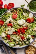 white bowl filled with Pesto chicken zoodle salad topped with fresh cherry tomatoes, pearl mozzarella and toasted pine nuts