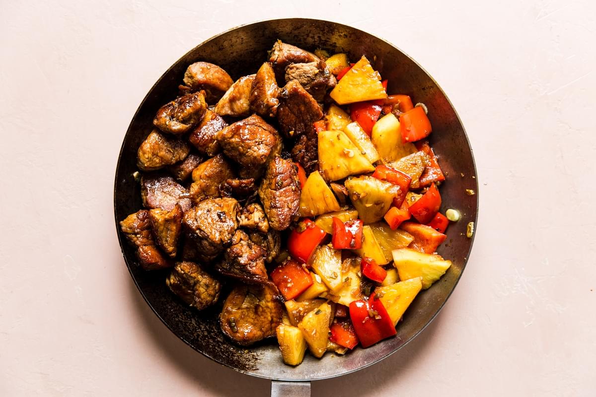 crispy pork bites with cooked pineapple and red bell peppers in a skillet